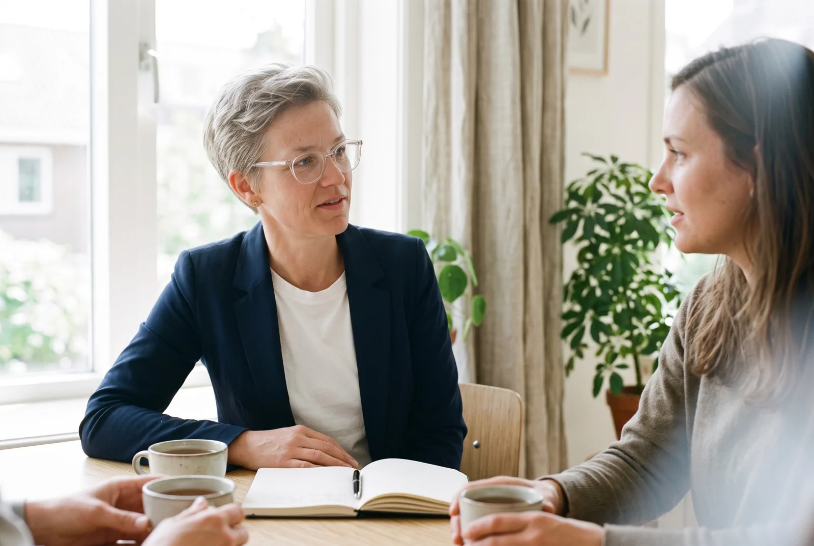 Lot in gesprek met een cliënt aan een houten tafel, twee koppen thee en een notitieboek